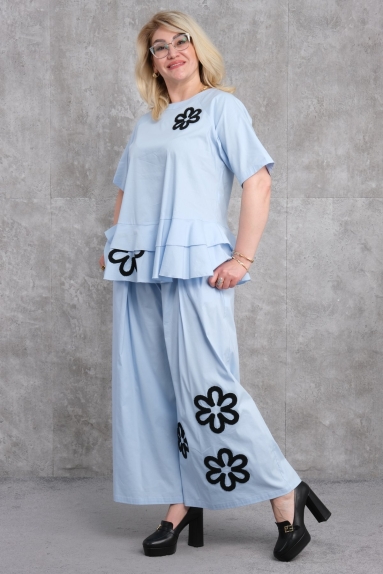  Этот двойной набор для женщин больших размеров, как видно на модели, сочетает в себе комфорт и стиль. Голубой костюм с волановыми деталями и черными цветочными принтами на верхней части представляет собой эффектный дизайн. Нижняя часть имеет широкие штанины и также украшена черными цветочными принтами, что придает яркий элемент. Изготовленный из 65% хлопка, 30% полиэстера и 5% эластана, продукт обеспечивает комфорт и долговечность. Доступен в размерах 42, 44, 46 и 48.