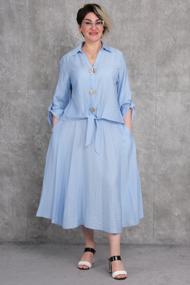  The product seen on the model is a plus size womens two-piece set in blue color. The set is available in sizes 42, 44, 46, and 48. The fabric composition is 65% cotton, 30% polyester, and 5% elastane. The top piece is designed with elegant flower detailed buttons and a tie at the waist. The bottom piece is a loose-fitting, comfortable skirt with pockets on both sides. This set combines elegance with comfort, adding sophistication to your daily wear.