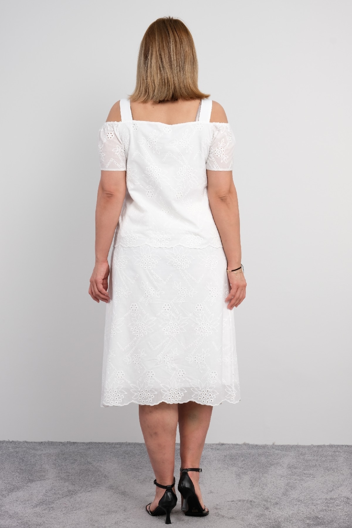  For plus size women, a two-piece suit consisting of a white colored, short-sleeved blouse with lace details and a long skirt.